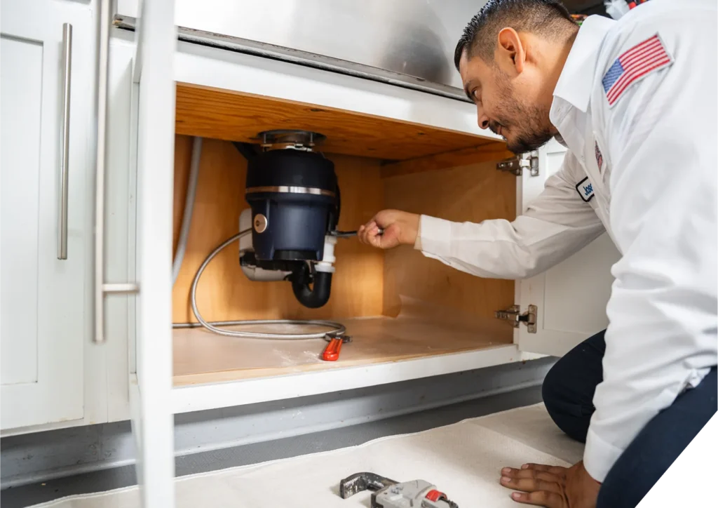 Reliable Home Comfort technician servicing a garbage disposal unit under a kitchen sink during a plumbing visit in Yorba Linda, CA.