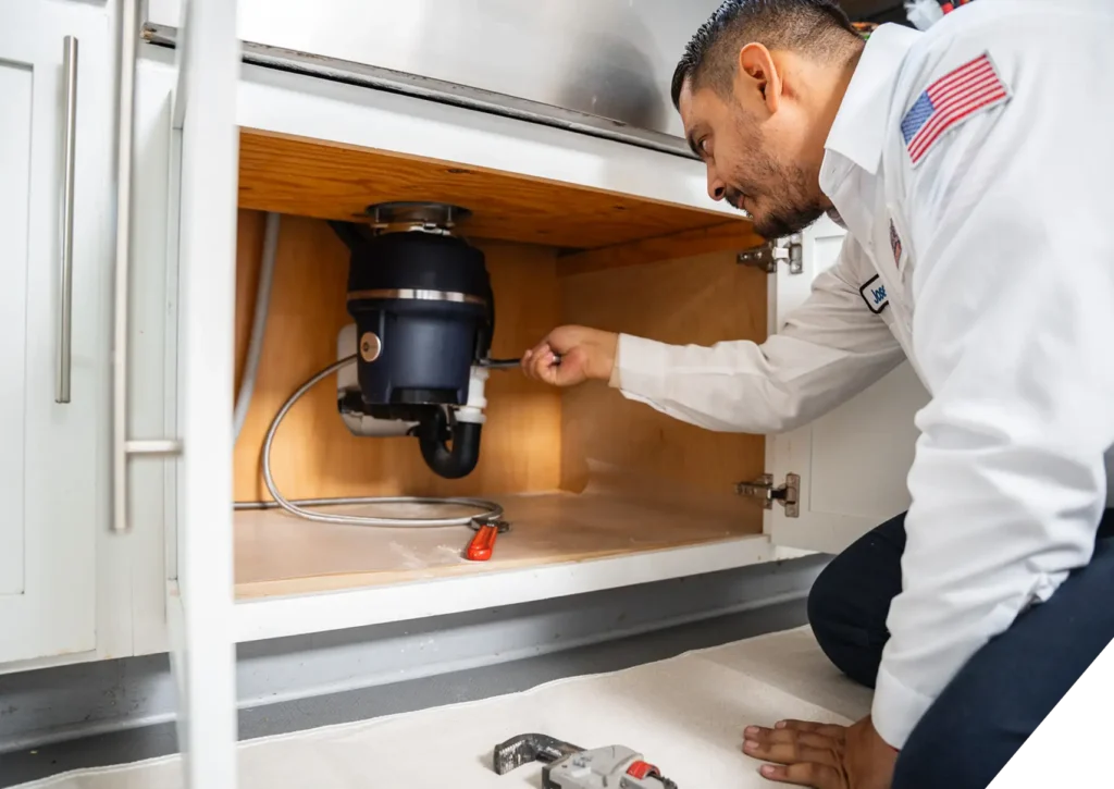 Technician from Reliable Home Comfort servicing a garbage disposal unit under a kitchen sink